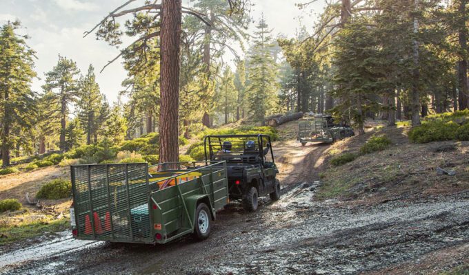 Kawasaki Mules with trailers making their way along a track through a forest